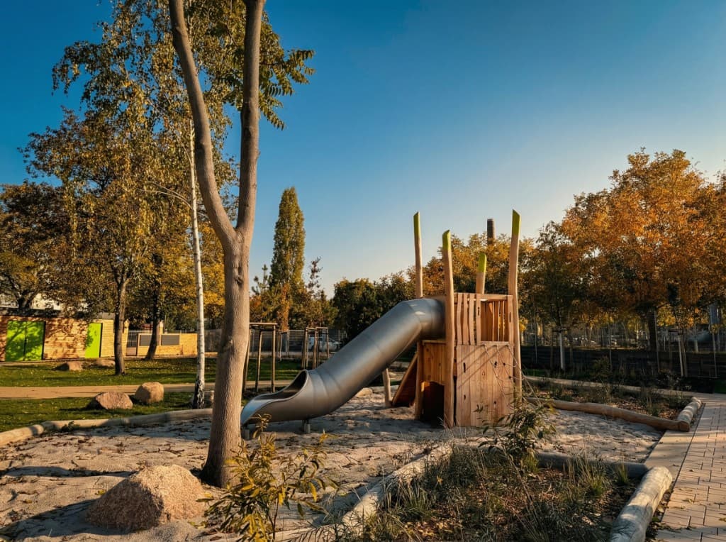 Kompakter Spielturm mit Röhrenrutsche in moderner Gestaltung, eingebettet in eine Parklandschaft